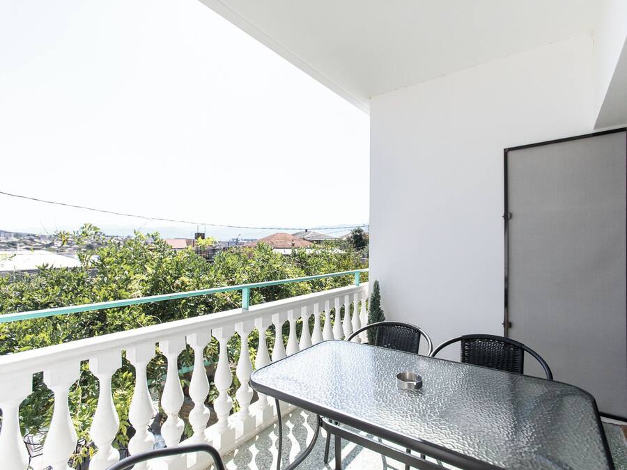Ein Balkon mit Glastisch und -stühlen, weißem Geländer und Blick auf eine Stadtlandschaft.