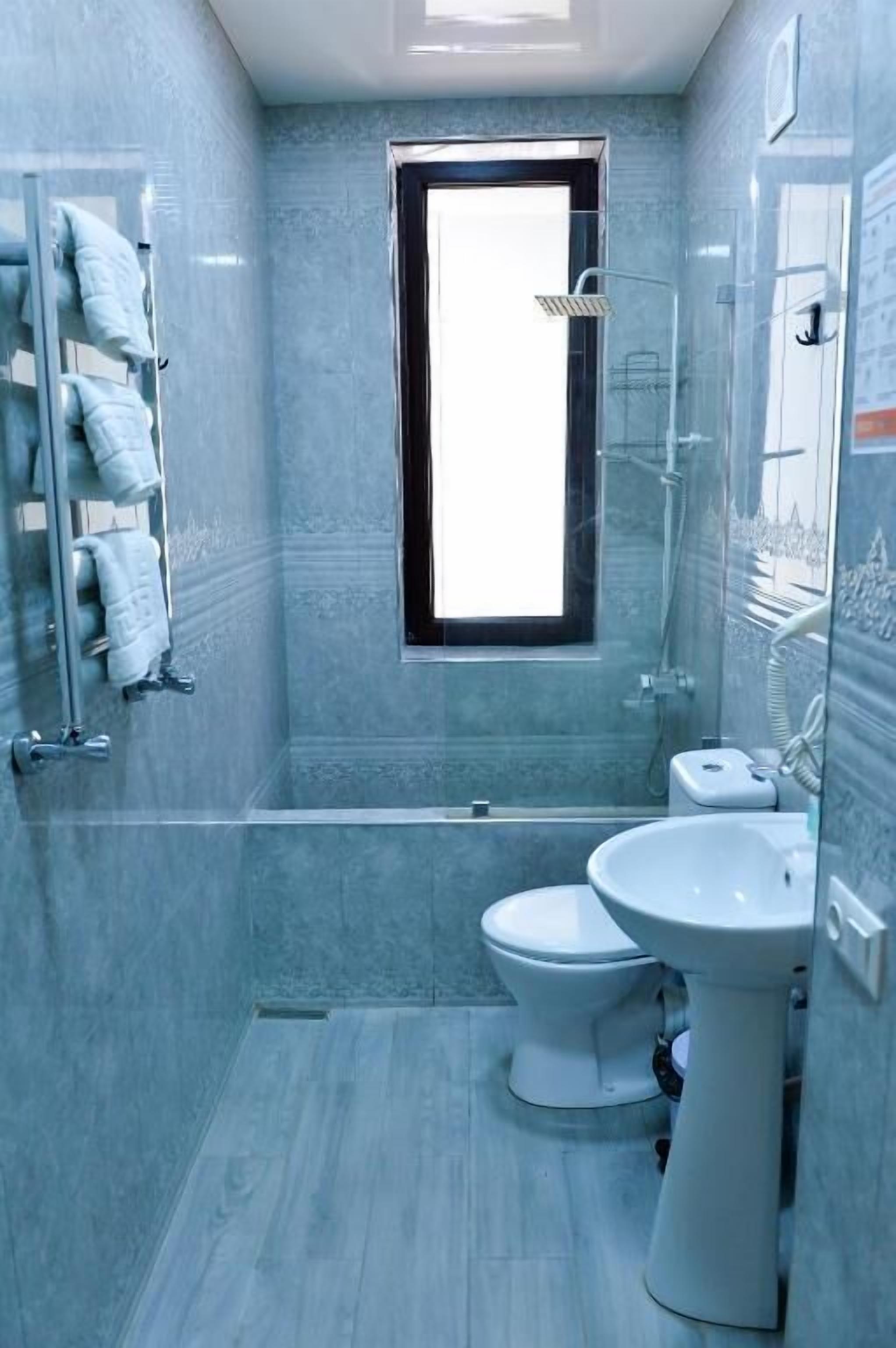 A compact bathroom with a shower, toilet, and sink, featuring a small window and a towel rack.