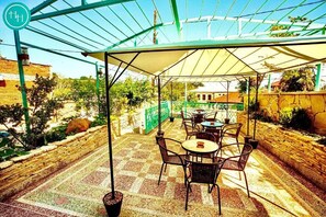 An outdoor patio with tables and chairs, a covered area with a transparent roof, and a stone wall. - Hotel History (Kutaisi)
