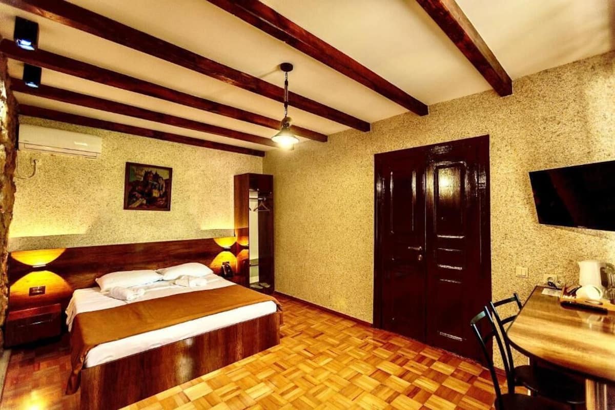 A hotel room with a wooden bed, a desk, and a television on the wall.