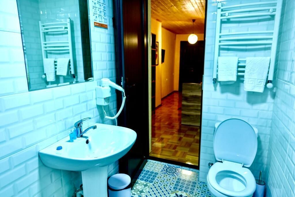 A bathroom with a white sink, a mirror, a toilet, and a patterned floor.