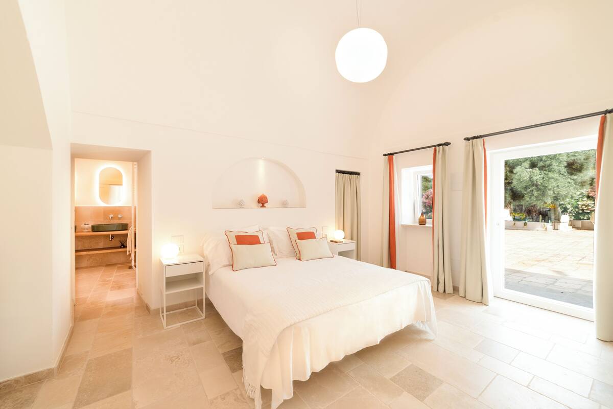 Un dormitorio con cama, mesitas de noche, lámpara de noche y vistas al exterior.