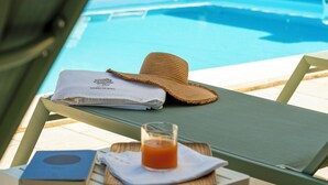 Uma espreguiçadeira à beira da piscina, com chapéu, toalha e um copo de suco de laranja.