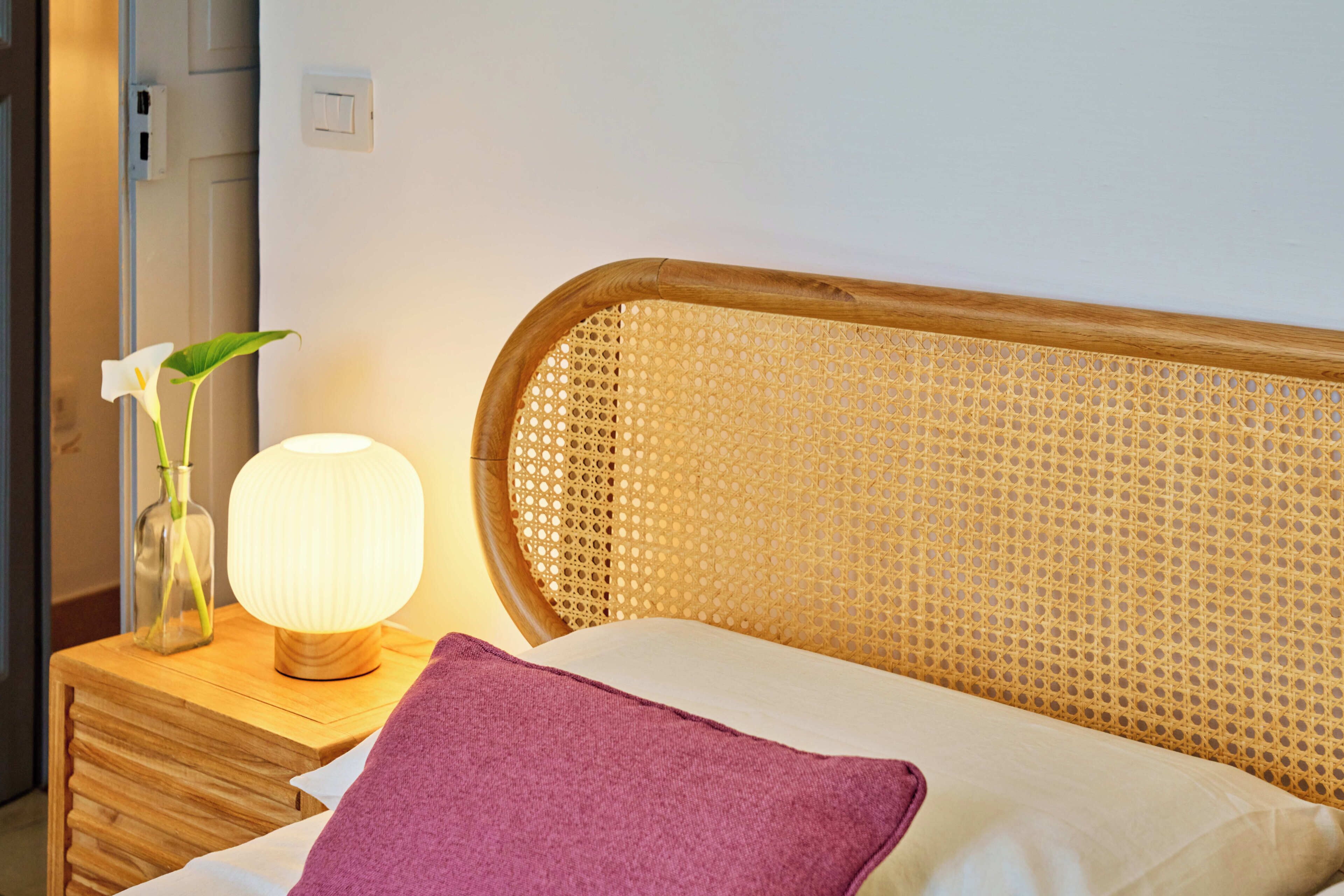 Un letto con una testiera in legno, un comodino con una lampada e un vaso con una pianta.