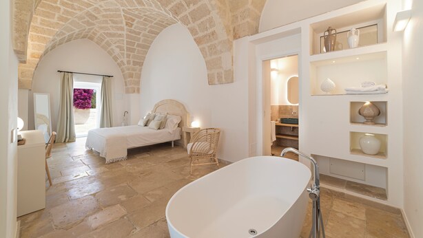 Um quarto espaçoso com uma cama grande, um espaço de estar com uma cadeira e um banheiro com banheira.