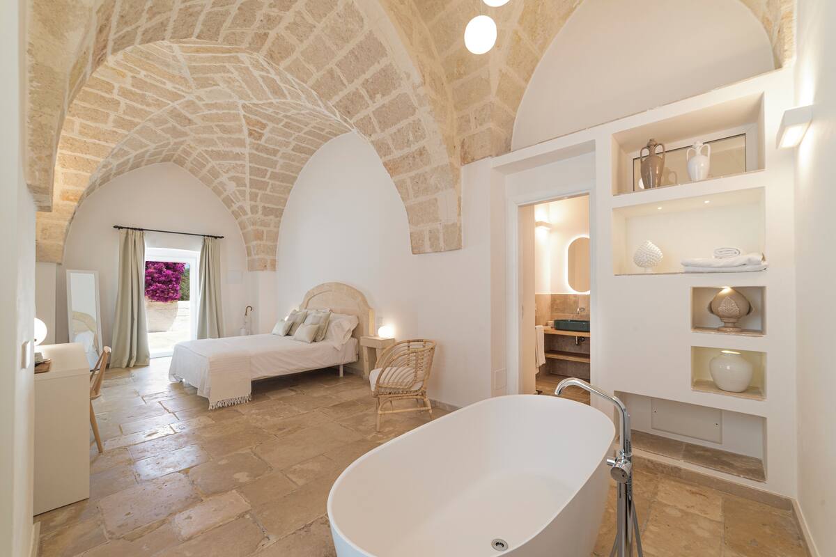 Un dormitorio espacioso con una cama grande, una zona de estar con un sillón y un baño con bañera.