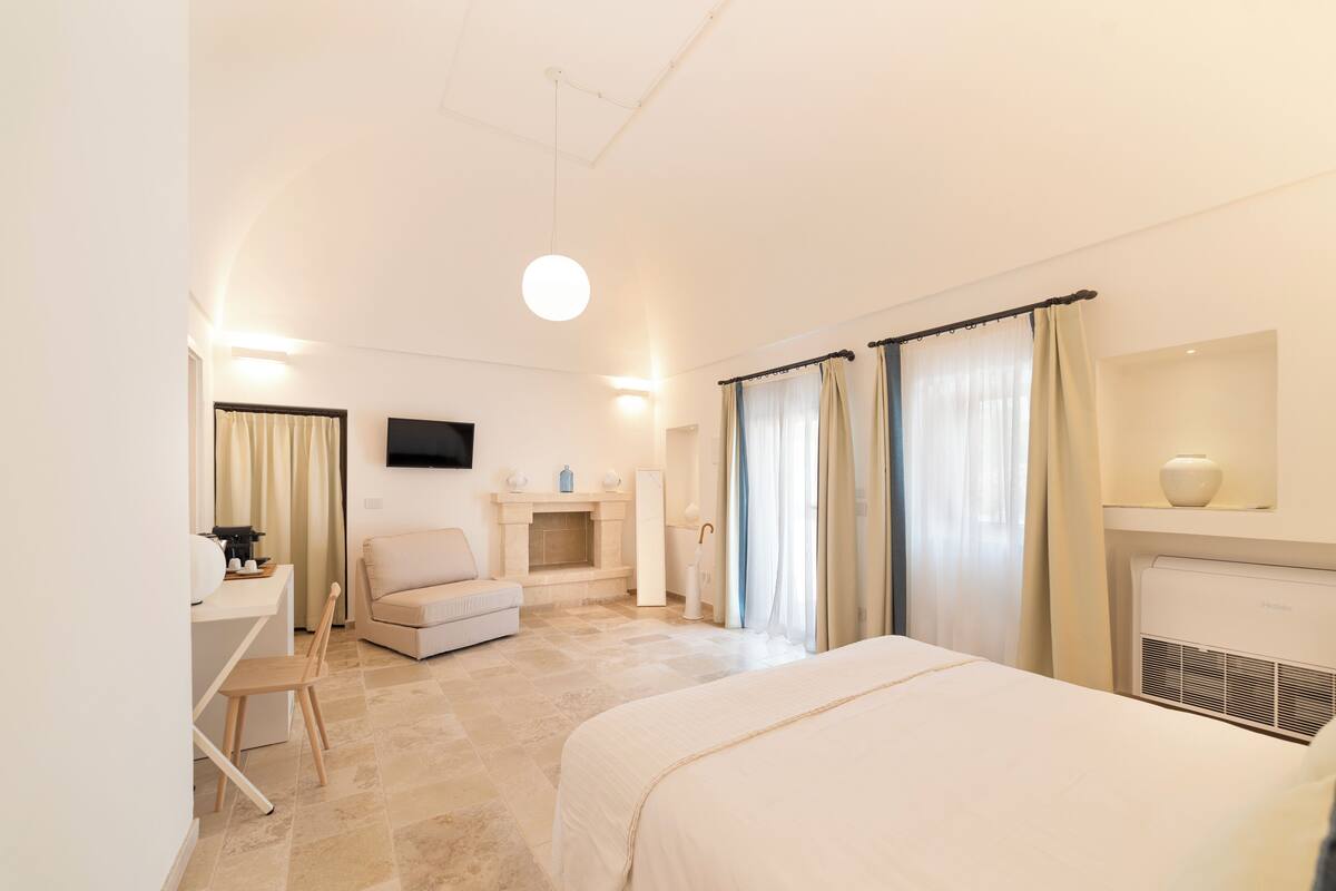 Habitación de hotel con cama, escritorio, silla, televisión, chimenea y cortinas.