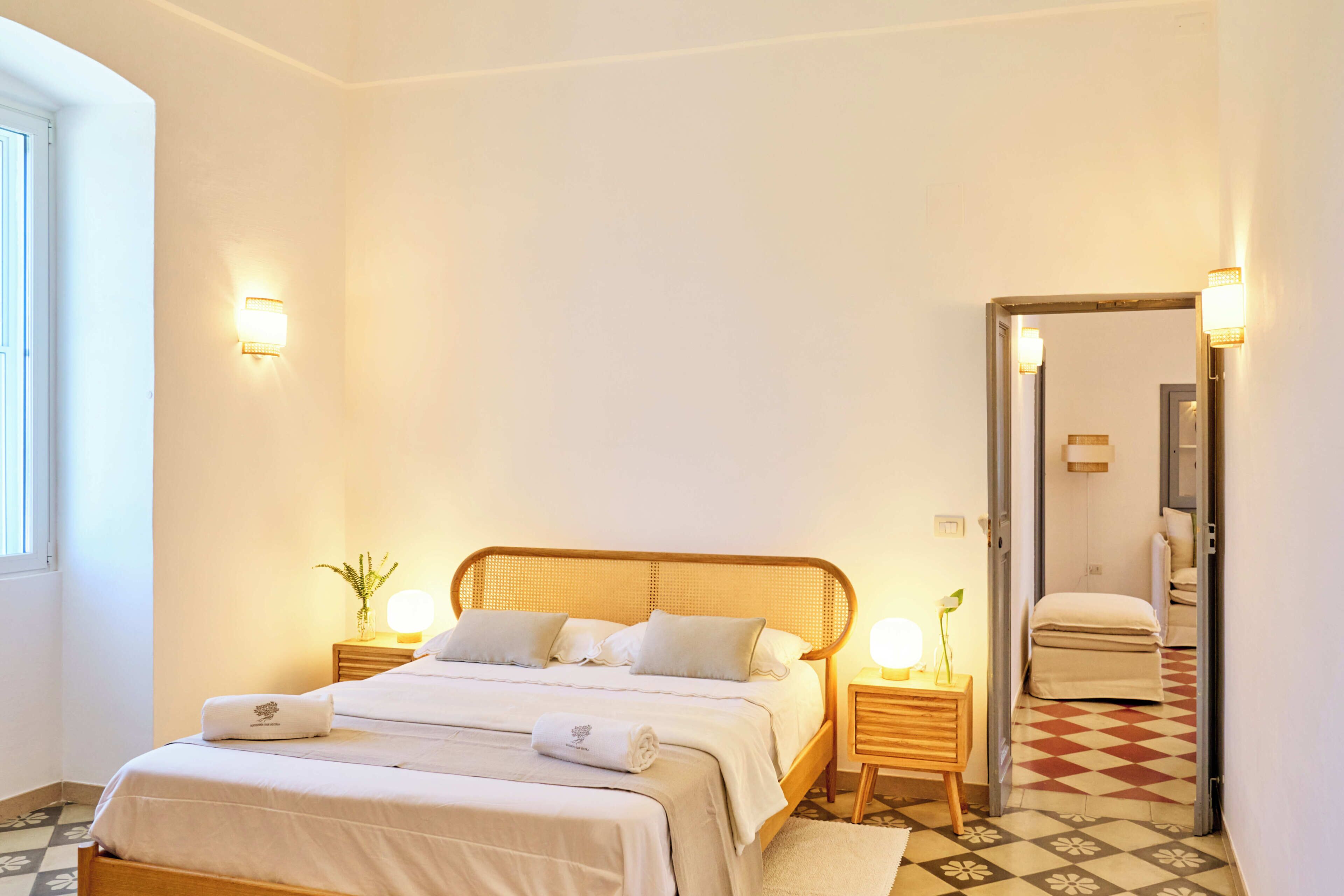 A hotel room with a large bed, bedside tables, a mirror, and a view of the hallway.