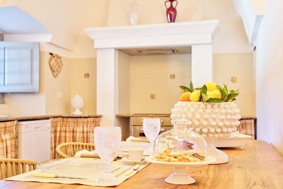 Una mesa de comedor dispuesta con cristalería, platos y un centro de mesa de frutas.