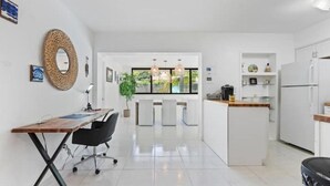 A modern kitchen with white cabinetry, a central island, and a dining area with a long table and chairs. - Tropical Beach House - Pool & Private Backyard - Close to everything (Boynton Beach)