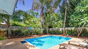 A swimming pool with a wooden deck, surrounded by palm trees and a wooden fence. - Tropical Beach House - Pool & Private Backyard - Close to everything (Boynton Beach)
