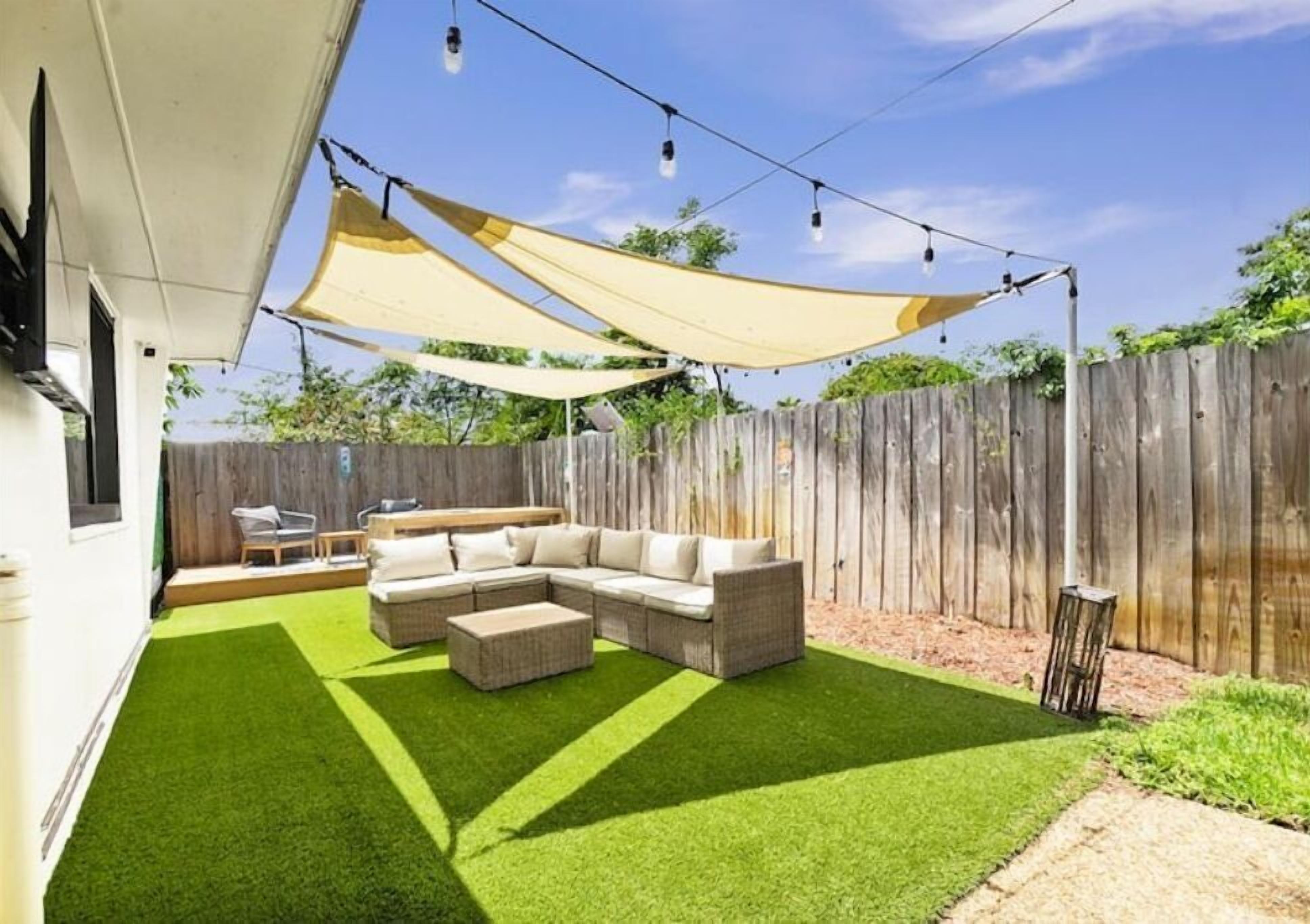 A backyard with artificial grass, a sectional sofa, and a wooden fence.