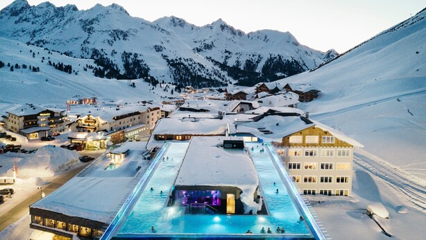Un complejo turístico en la montaña cubierto de nieve, con piscina y edificios.
