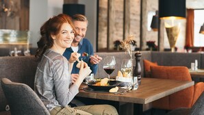 Una pareja cenando en un restaurante con una mesa de madera, copas de vino y un jarrón con flores secas.