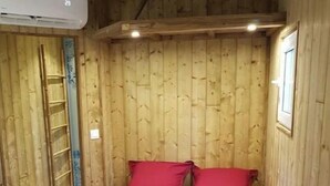A small, wooden room with a bed, a ladder, and an air conditioning unit. - Logement Atypique (Le diamant)