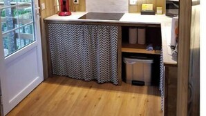 A compact kitchen with wooden walls, a sink, a small countertop, and a window. - Logement Atypique (Le diamant)