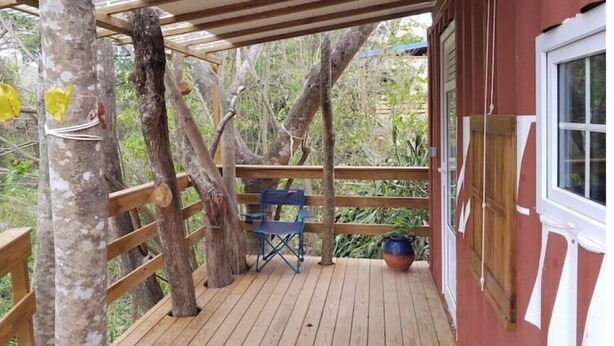 A wooden deck with a blue folding chair and a potted plant, surrounded by trees. - Logement Atypique (Le diamant)