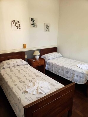 A hotel room with two single beds, a wooden headboard, a nightstand with a lamp, and wall art.