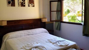 Une chambre à coucher avec un lit, un ventilateur de plafond, une fenêtre avec des rideaux et des œuvres d’art murales.