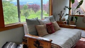 Un dormitorio con un ventanal grande, un cabecero de madera y vistas al exterior con vegetación.