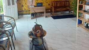 A room with a tiled floor, wicker furniture, a laptop on a table, and a wall with two large paintings.