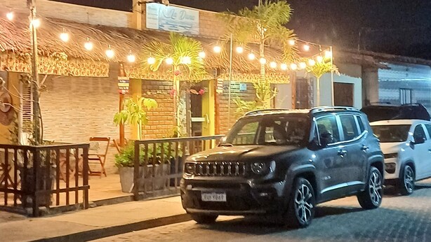 A building with a brick facade, outdoor seating area with tables and chairs, and a parked SUV.