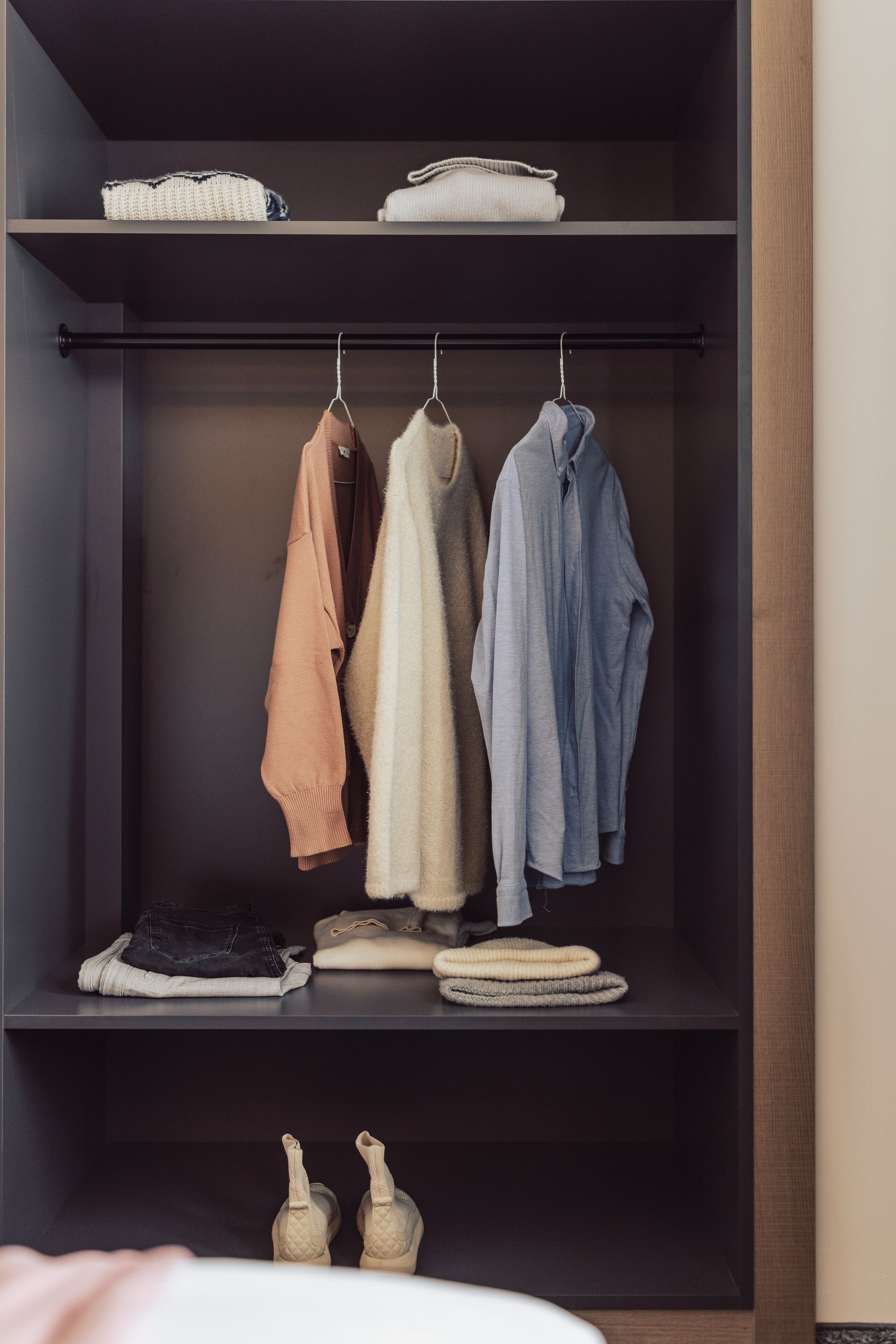 A closet with hanging clothes, folded items, and shoes.