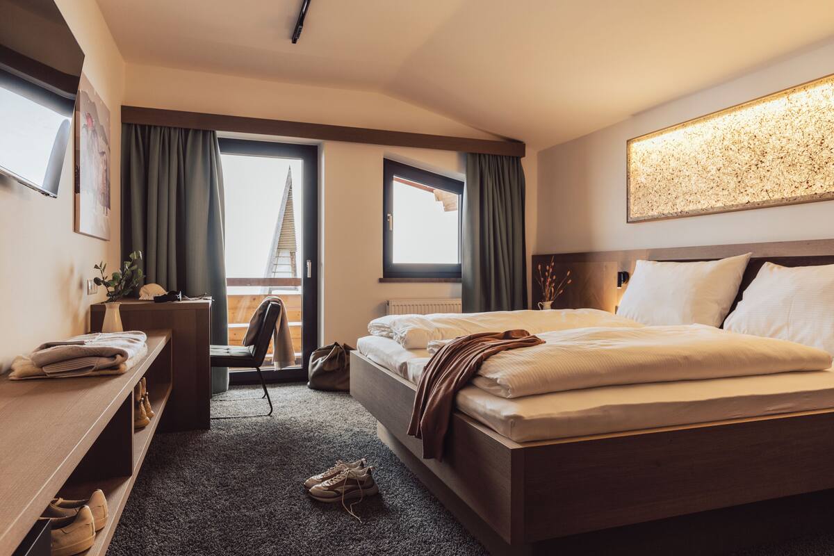 A hotel room with a large bed, a desk, a chair, and a view of a building through a window.