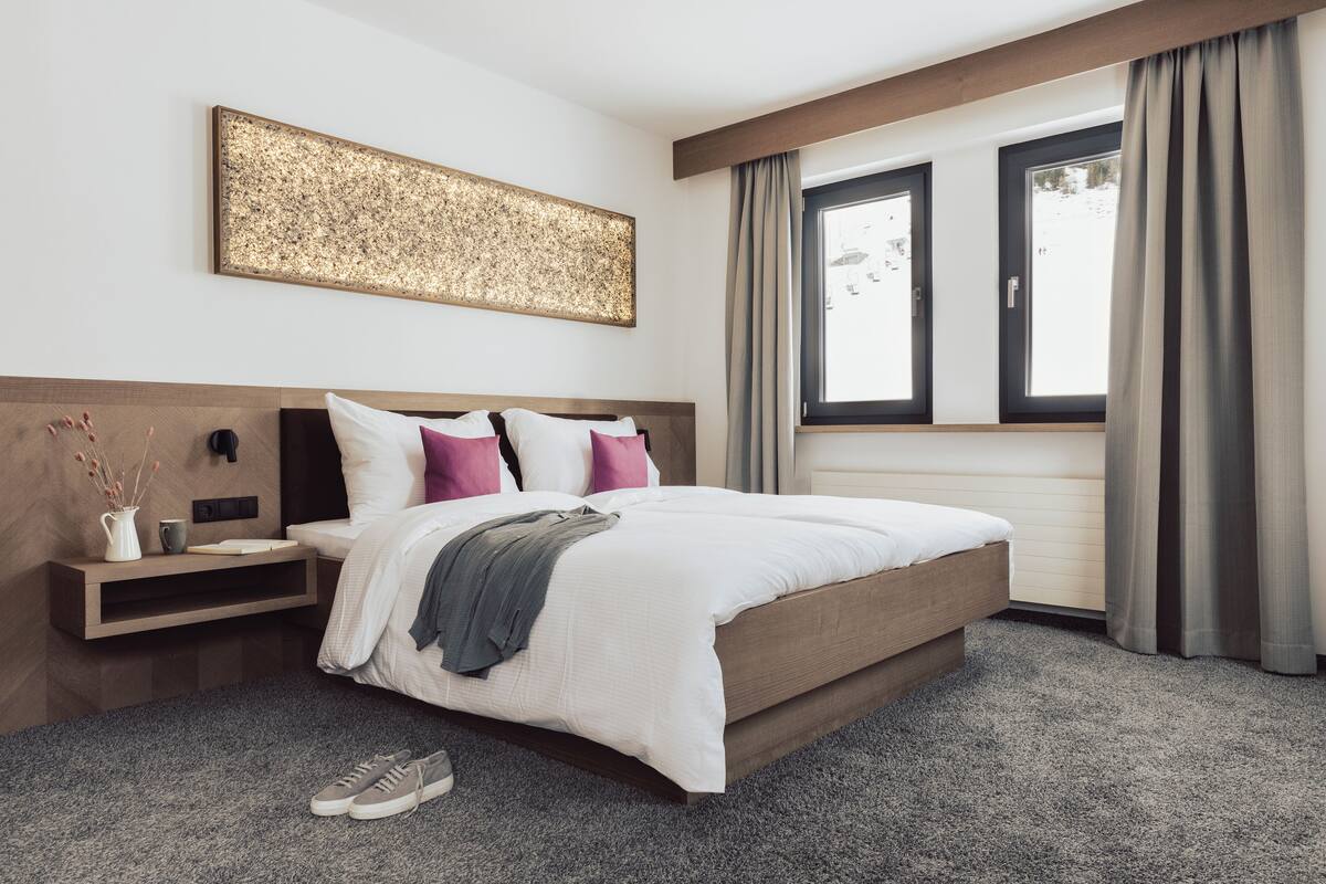 A modern hotel room with a large bed, a nightstand, a wall-mounted artwork, and a window with curtains.