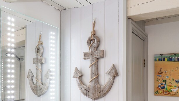A bathroom with a large mirror, a wooden anchor decoration, and a colorful painting on the wall. - Madelines View (Whitby)
