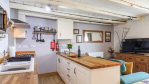 A compact kitchen with a stove, sink, and wooden countertop. There is a fire extinguisher, a mirror, and a television on a wooden cabinet. - Madelines View (Whitby)