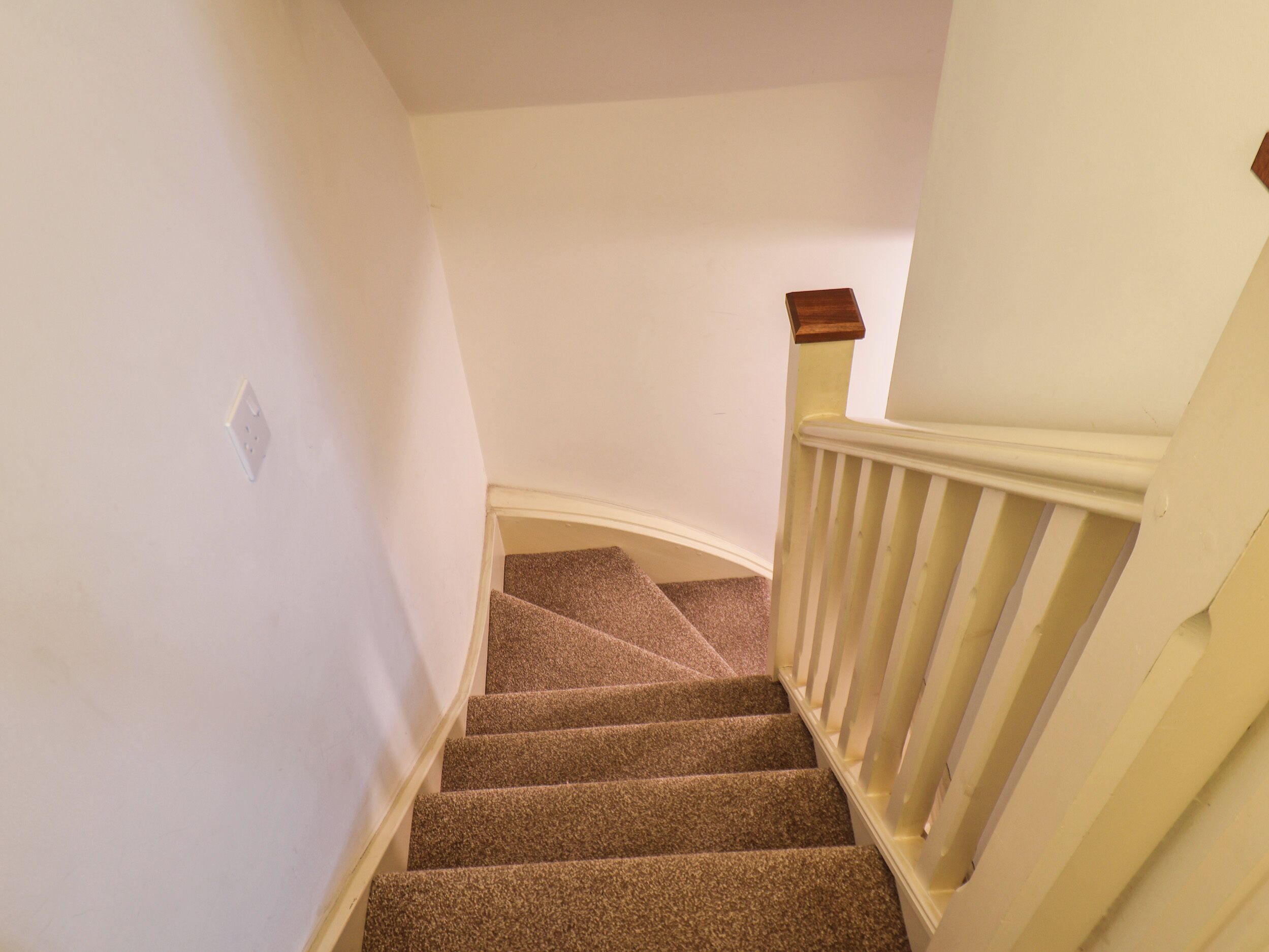 Un escalier recouvert de moquette, avec des rampes blanches et une main courante en bois.