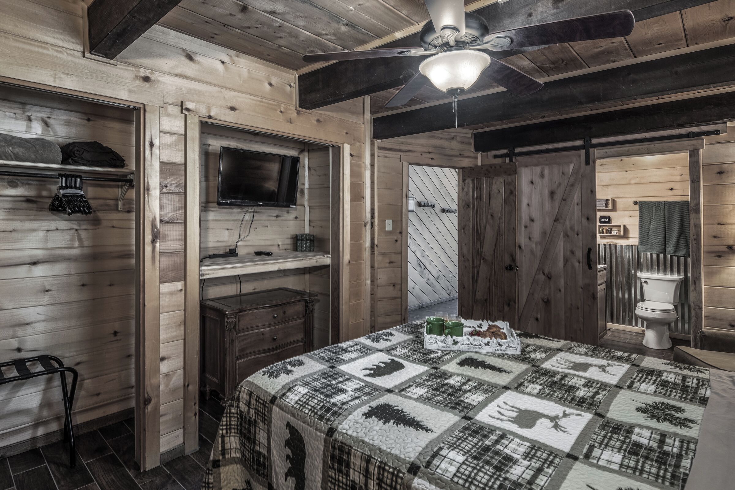 Interior de una cabaña de madera con cama, televisor y baño.