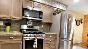 A kitchen with stainless steel appliances, wooden cabinets, and a tiled backsplash.