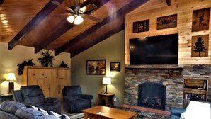 A cozy living room with a fireplace, leather sofas, a wooden coffee table, and a ceiling fan.