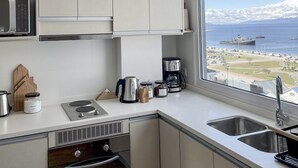 Una cuina moderna amb armaris blancs, un microones integrat, una cafetera i vista a un port amb vaixells.