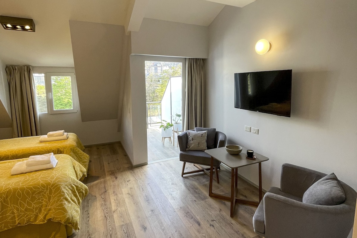 Ein Hotelzimmer mit Bett, Schreibtisch, Sessel, Fernseher und Blick ins Freie.
