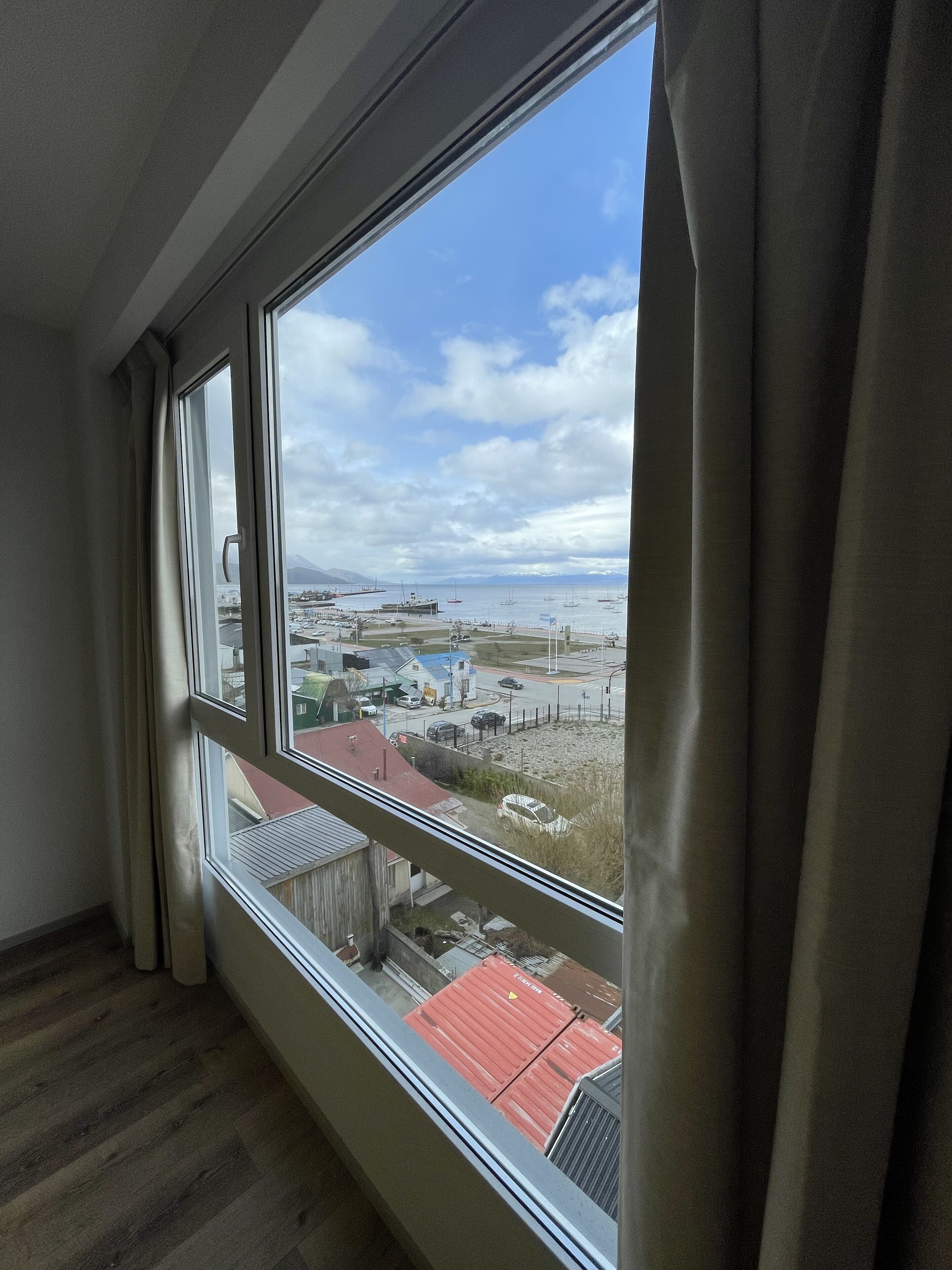 A room with a large window overlooking a marina and distant mountains.