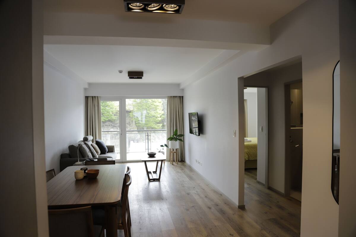 Ein geräumiger Wohnbereich mit Esstisch, Sofa und großem Fenster mit Vorhängen.
