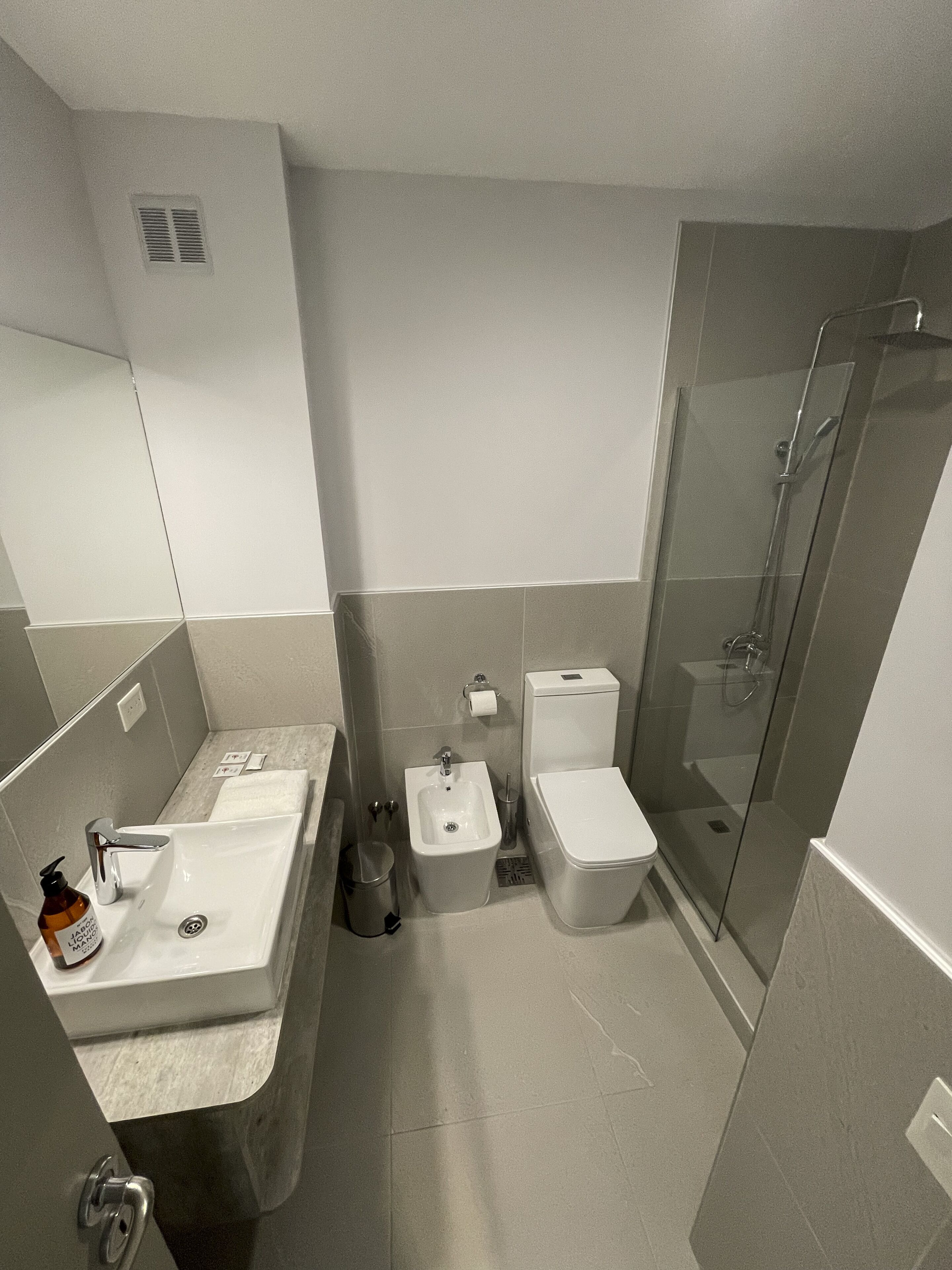Et moderne badeværelse med stor vask, bidet, toilet og brusebad med glasvægge.