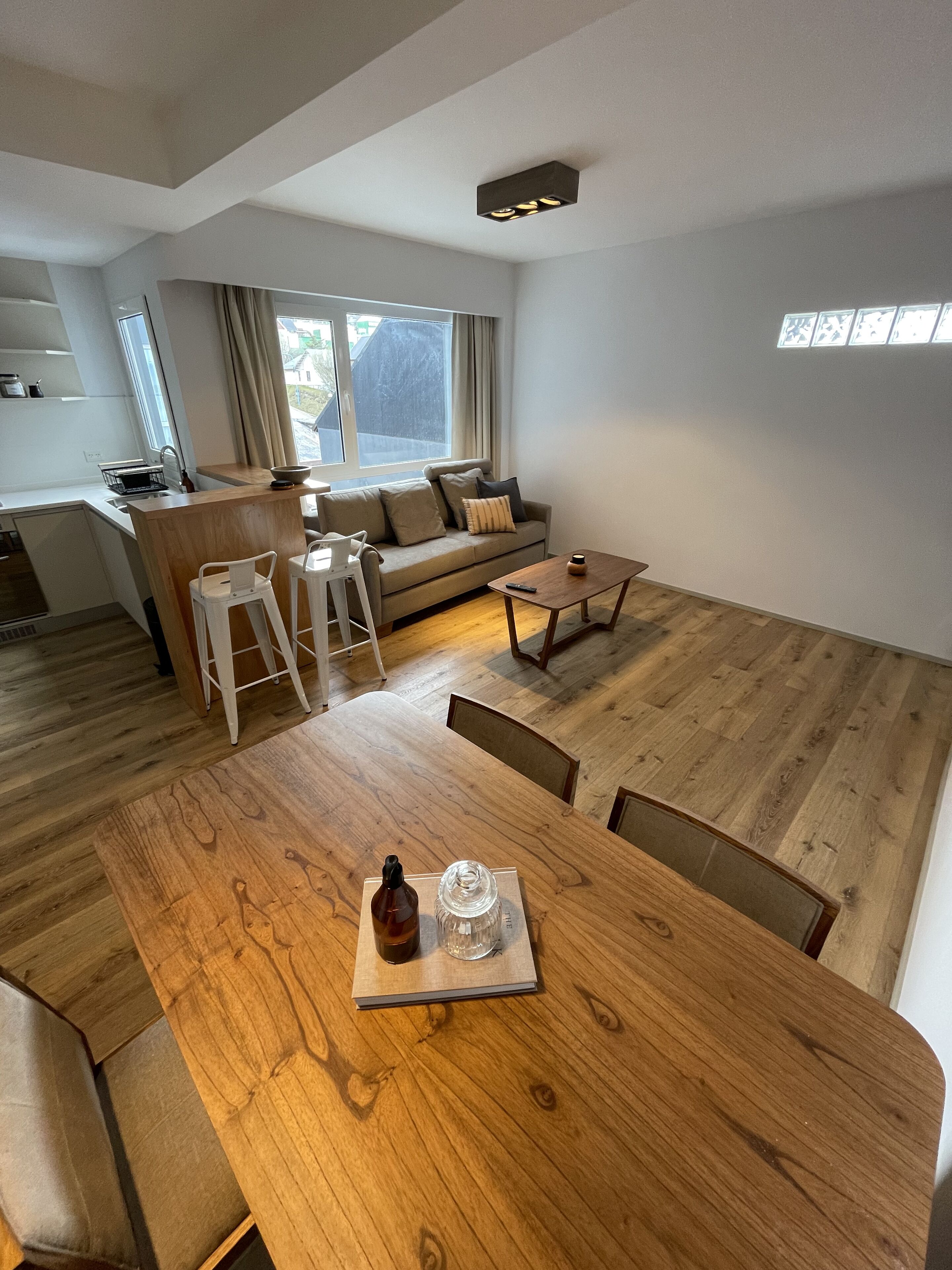 A modern living room with a wooden dining table, a sofa, and a kitchen area.