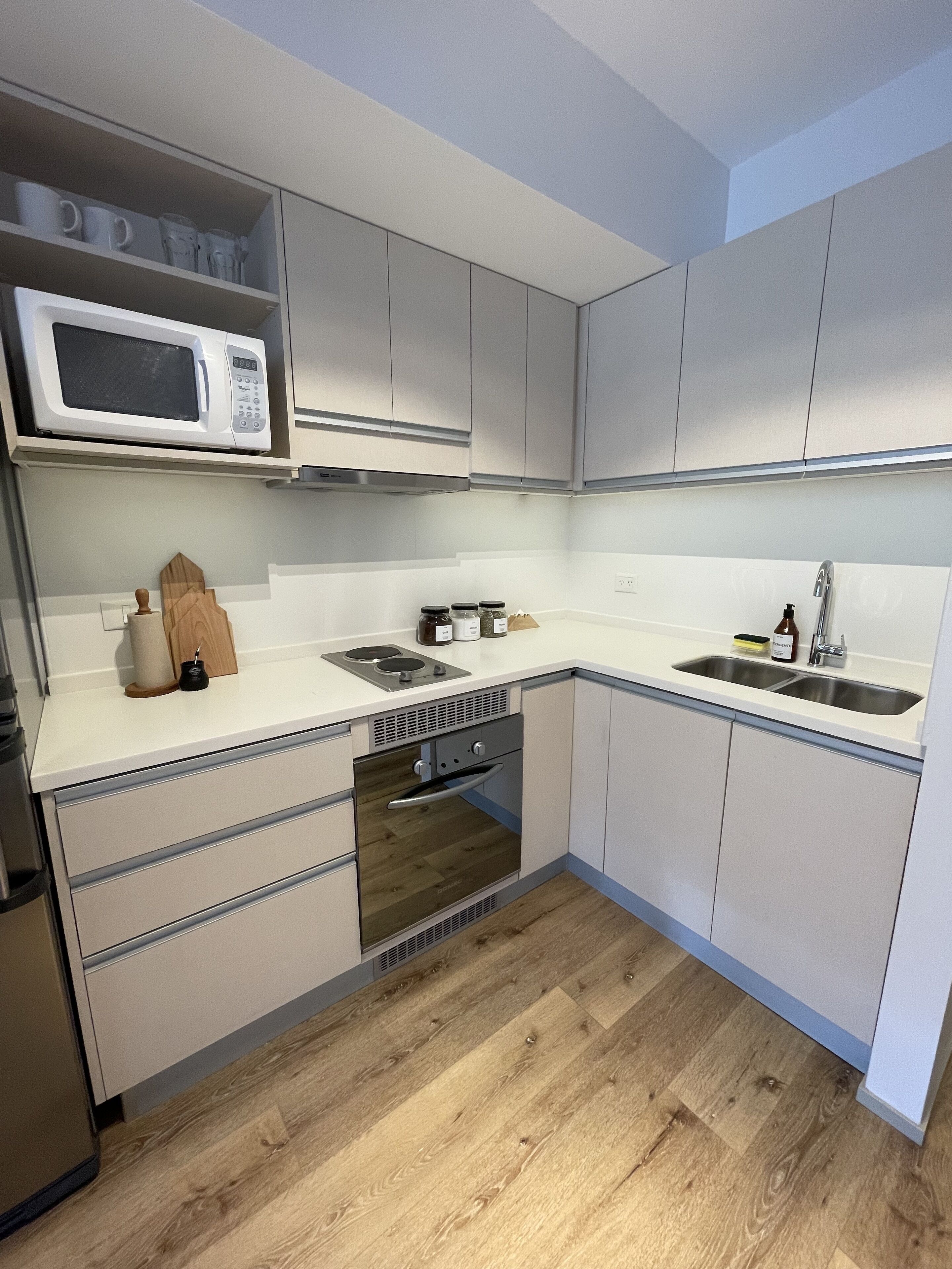 Een moderne keuken met witte kastjes, een ingebouwde magnetron, een spoelbak en een houten vloer.