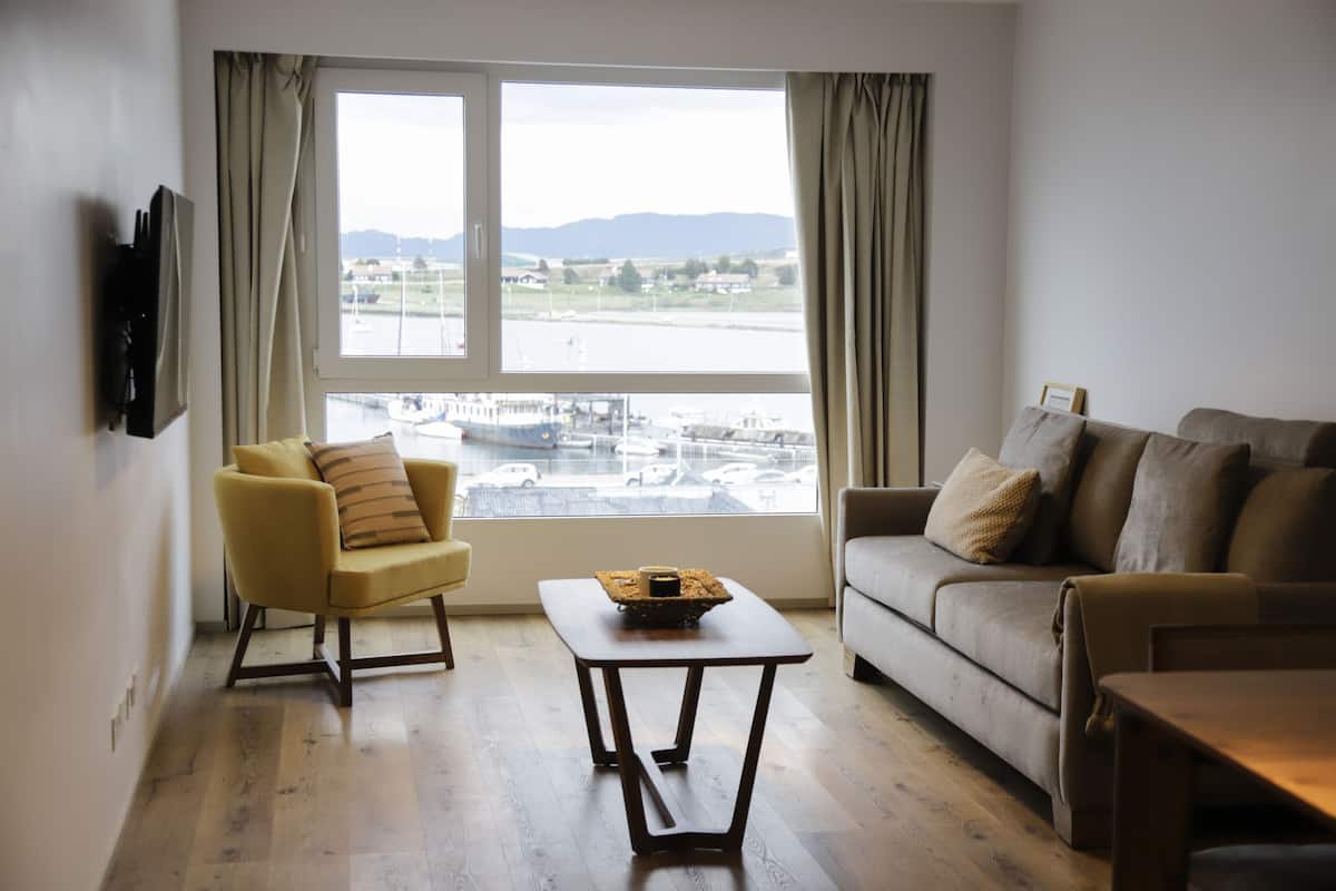 Ein Wohnzimmer mit einer Couch, einem Sessel, einem Couchtisch und einem an der Wand befestigten Fernseher.