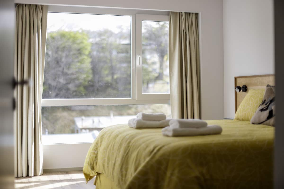 Ein Hotelzimmer mit Bett, einem Fenster mit Vorhängen und Blick auf Bäume.
