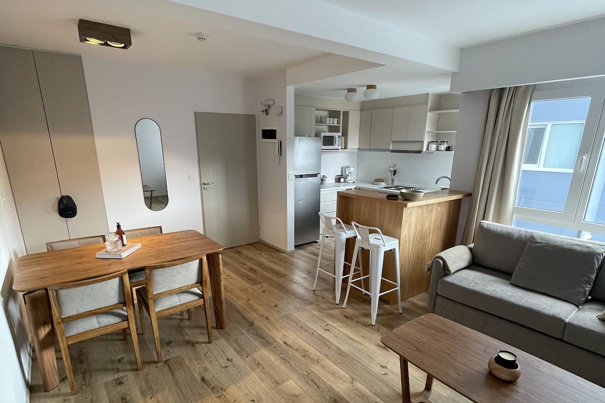 Eine moderne Wohnung mit Esstisch aus Holz, einer Couch und einer Küchenzeile.