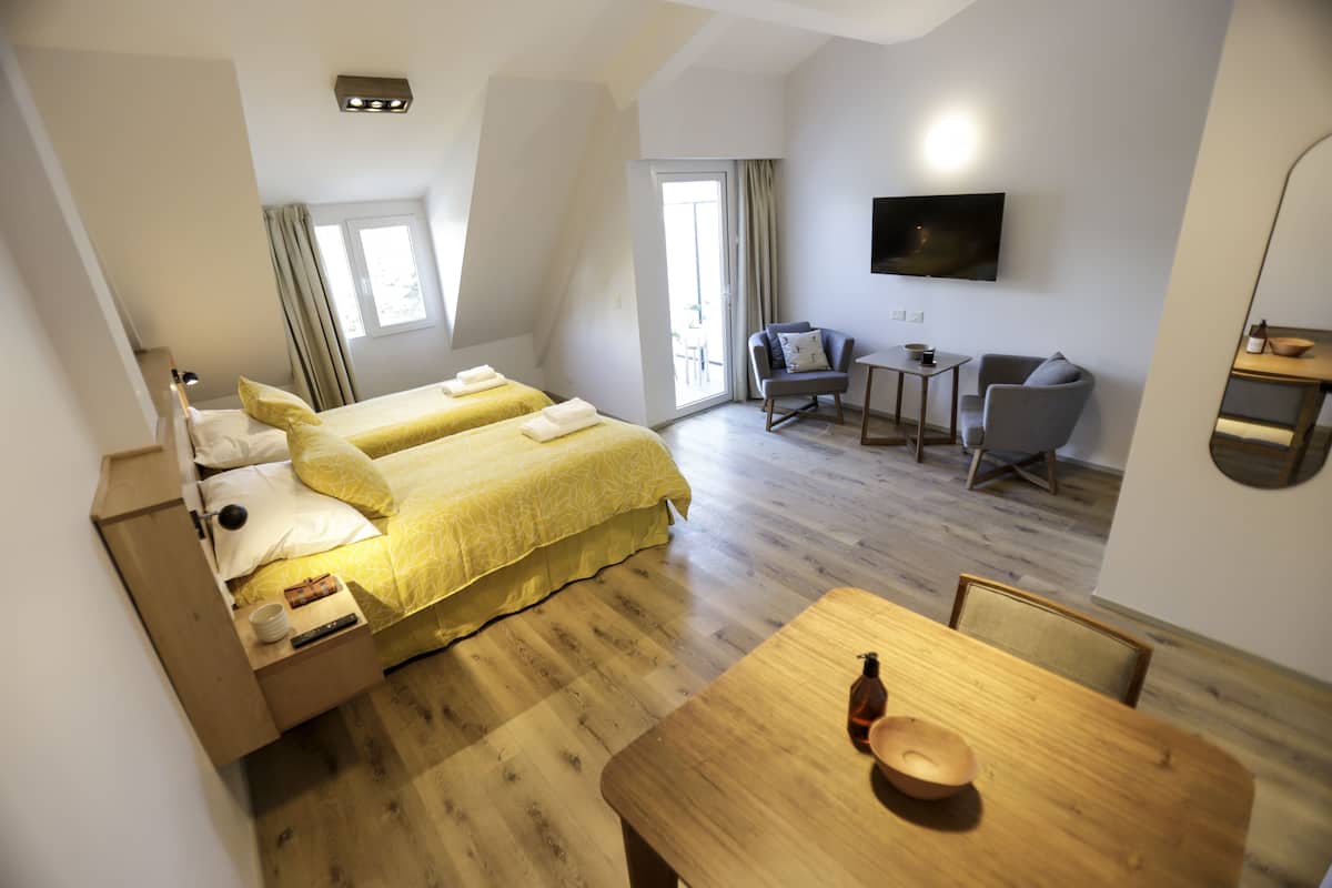 Ein modernes Hotelzimmer mit zwei Betten, einem Esstisch, einem Fernseher und einem Balkon.