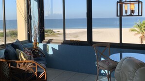 Una stanza con vista sulla spiaggia, una sedia in vimini, un tavolino e una lampada a sospensione.