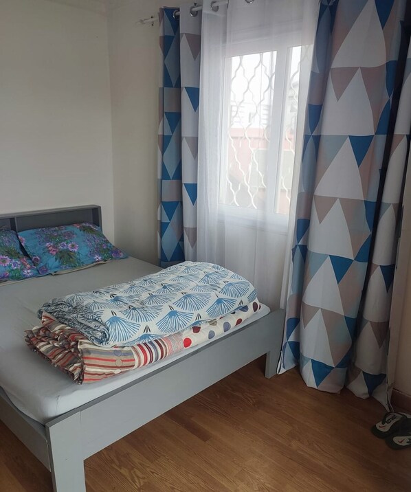 Una cama bien hecha con ropa de cama estampada, cabecera y ventana con cortinas geométricas.