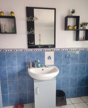 A bathroom with a white sink, blue tiles, a mirror, and shelves with toiletries. - Villa Saphira (Antananarivo)