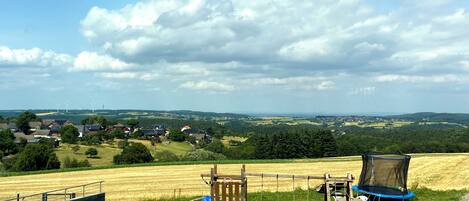 A playground with a slide and swings, surrounded by fields and houses in a rural setting.